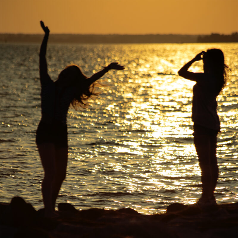 Showing two women silhouetted against the glistening water at sunset.