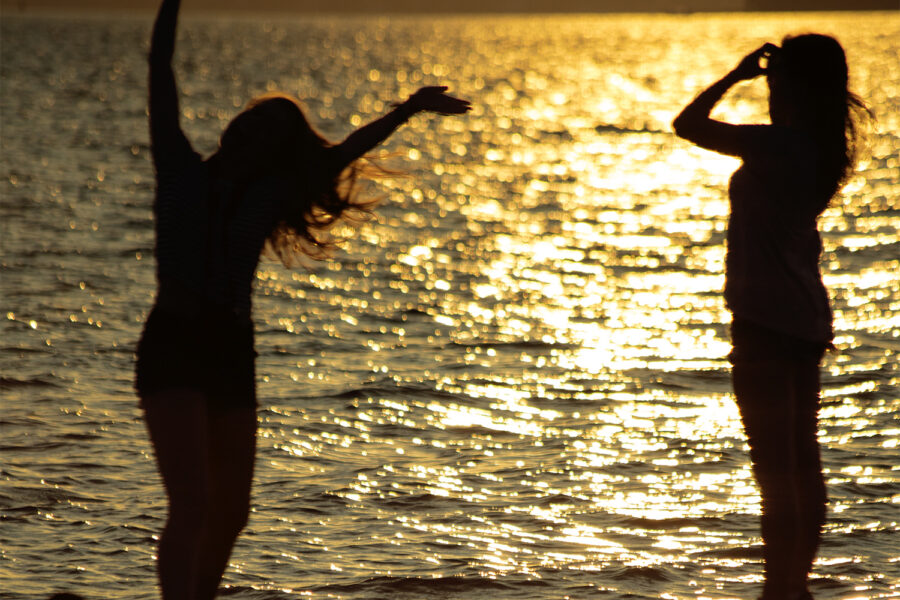Showing two women silhouetted against the glistening water at sunset.