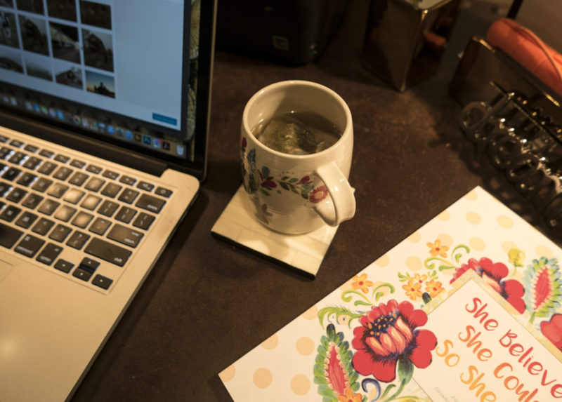 Showing a cup of tea positioned next to a motivational book and a computer.