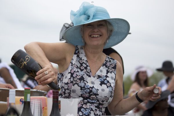 Showing a woman in a blue derby hat, pouring a bottle of champagne.